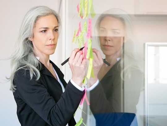 Content gray-haired Caucasian businesswoman writing on sticker