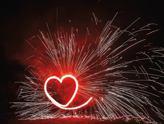 red heart shaped firework with sparkles on black background in n